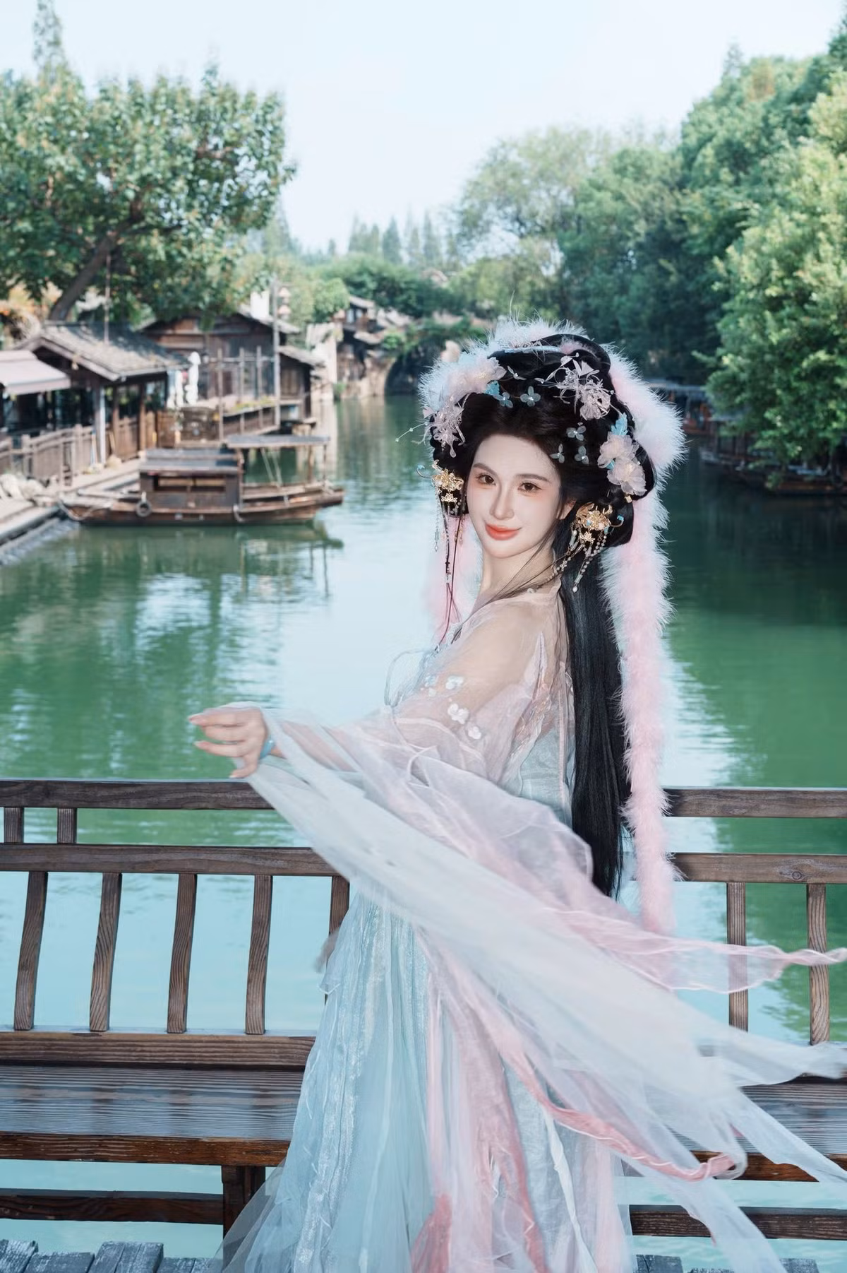 Điểm nhấn đắt giá nhất phải kể đến phần tạo hình tỉ mỉ. Mái tóc búi cao được trang hoàng bằng vô số trâm cài vàng và lông vũ hồng cầu kỳ, tạo nên một tổng thể vừa kiều diễm vừa quyền quý. (Ảnh: FBNV)