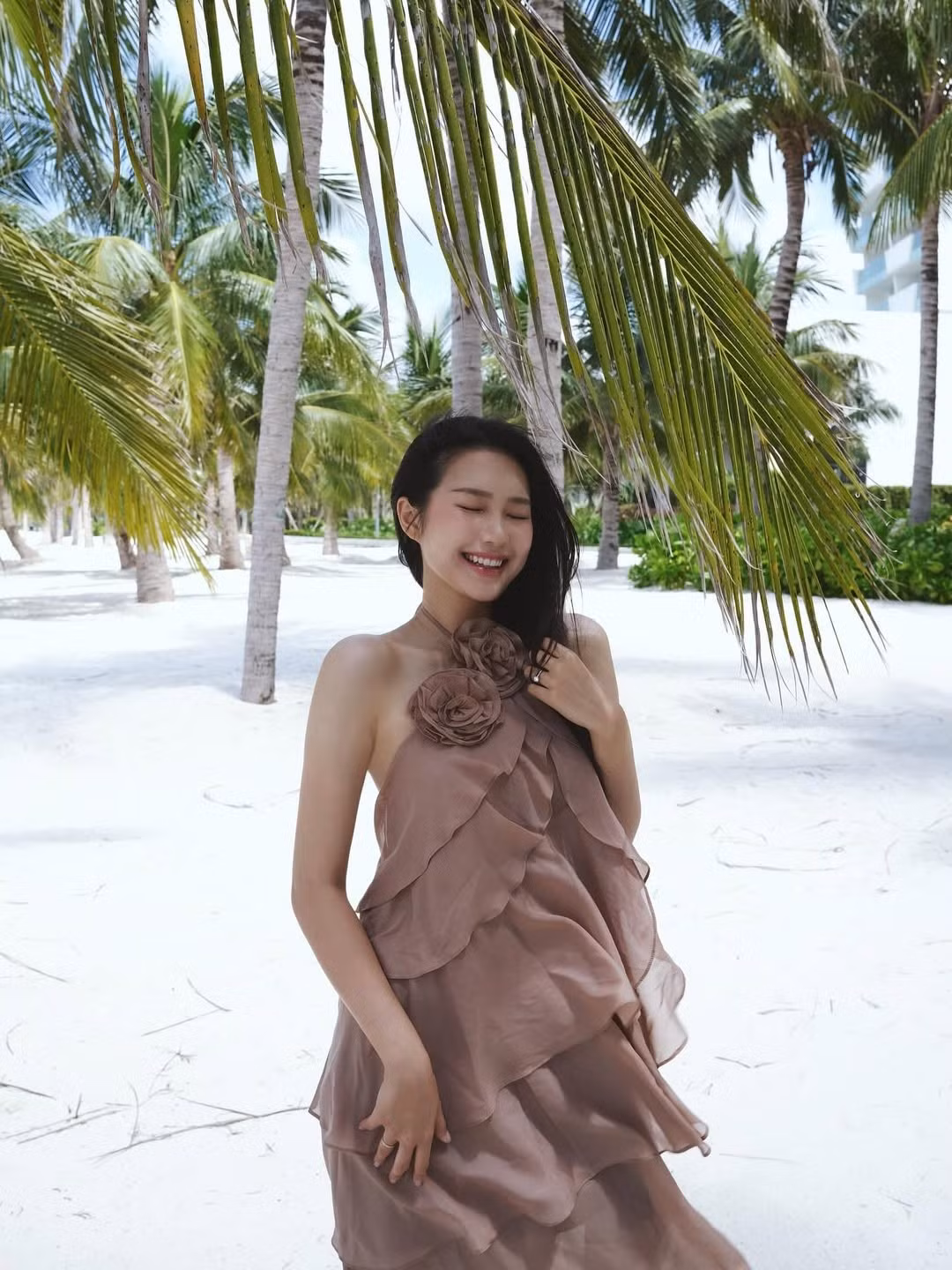 Mái tóc đen dài óng ả buông xõa tự nhiên, vài sợi tóc khẽ bay trong gió, nàng WAG tạo dáng đơn giản, khi thì tựa vào thân cây dừa, lúc lại cười rạng rỡ, đem đến cảm giác thư thái và mềm mại.