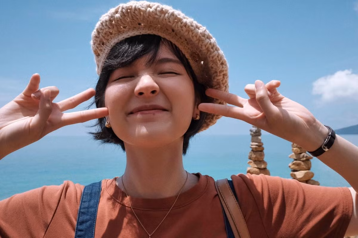 Cô lựa chọn chiếc áo thun màu nâu đất kết hợp cùng quần yếm jeans ống rộng thời thượng. Điểm nhấn cho trang phục là chiếc mũ cói đan và túi cói cỡ lớn, tạo nên tổng thể hài hòa, năng động.