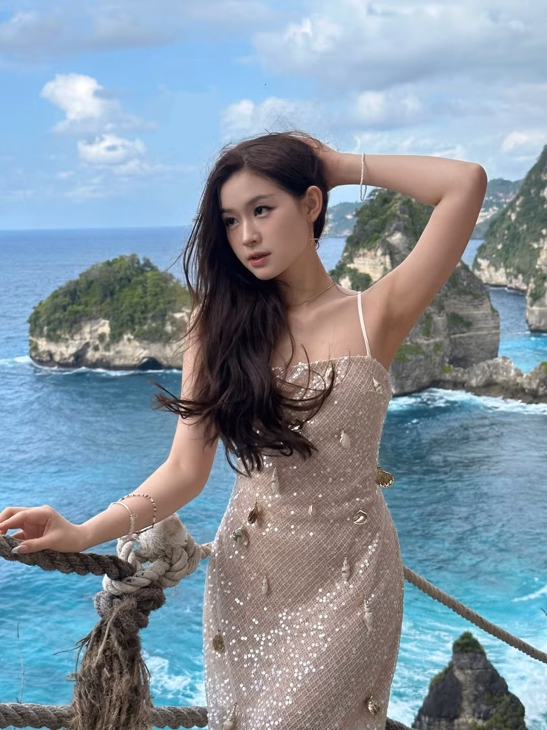 Trong loạt ảnh khác, Mai Hương chọn chiếc váy sequin lấp lánh màu nude, thiết kế hai dây đơn giản nhưng đủ tôn lên bờ vai thon thả và xương quai xanh quyến rũ. Đặc biệt, chiếc váy còn được đính kết những vỏ sò nhỏ xinh, tạo điểm nhấn độc đáo và rất phù hợp với không gian biển cả xanh biếc hùng vĩ phía sau.