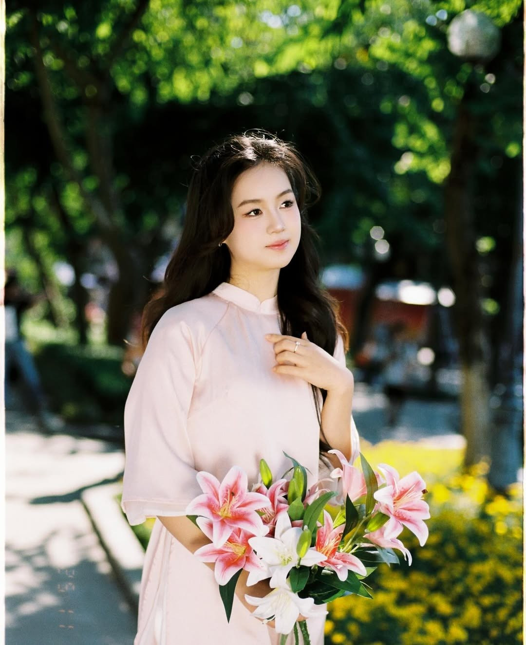 Cô nàng chọn chiếc áo dài màu hồng phấn nhẹ nhàng, nền nã, kết hợp với quần lụa trắng, tôn lên nét duyên dáng, dịu dàng của người con gái Việt Nam. Tay áo lỡ cánh sen tạo cảm giác thanh thoát, cổ áo đứng kín đáo toát lên vẻ trang nhã, hiện đại. (Ảnh: IGNV)