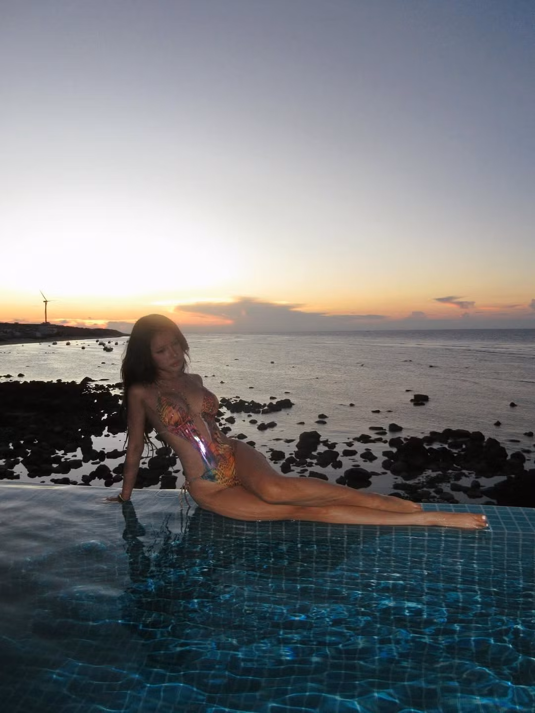 Xuân Ca đã chọn thời điểm "giờ vàng" (golden hour) khi mặt trời vừa lặn, tạo nên một phông nền rực rỡ với sắc cam, hồng, tím hòa quyện. Ánh sáng tự nhiên này không chỉ tôn lên làn da rám nắng khỏe khoắn của cô mà còn tạo hiệu ứng đổ bóng nghệ thuật. (Ảnh: IGNV)