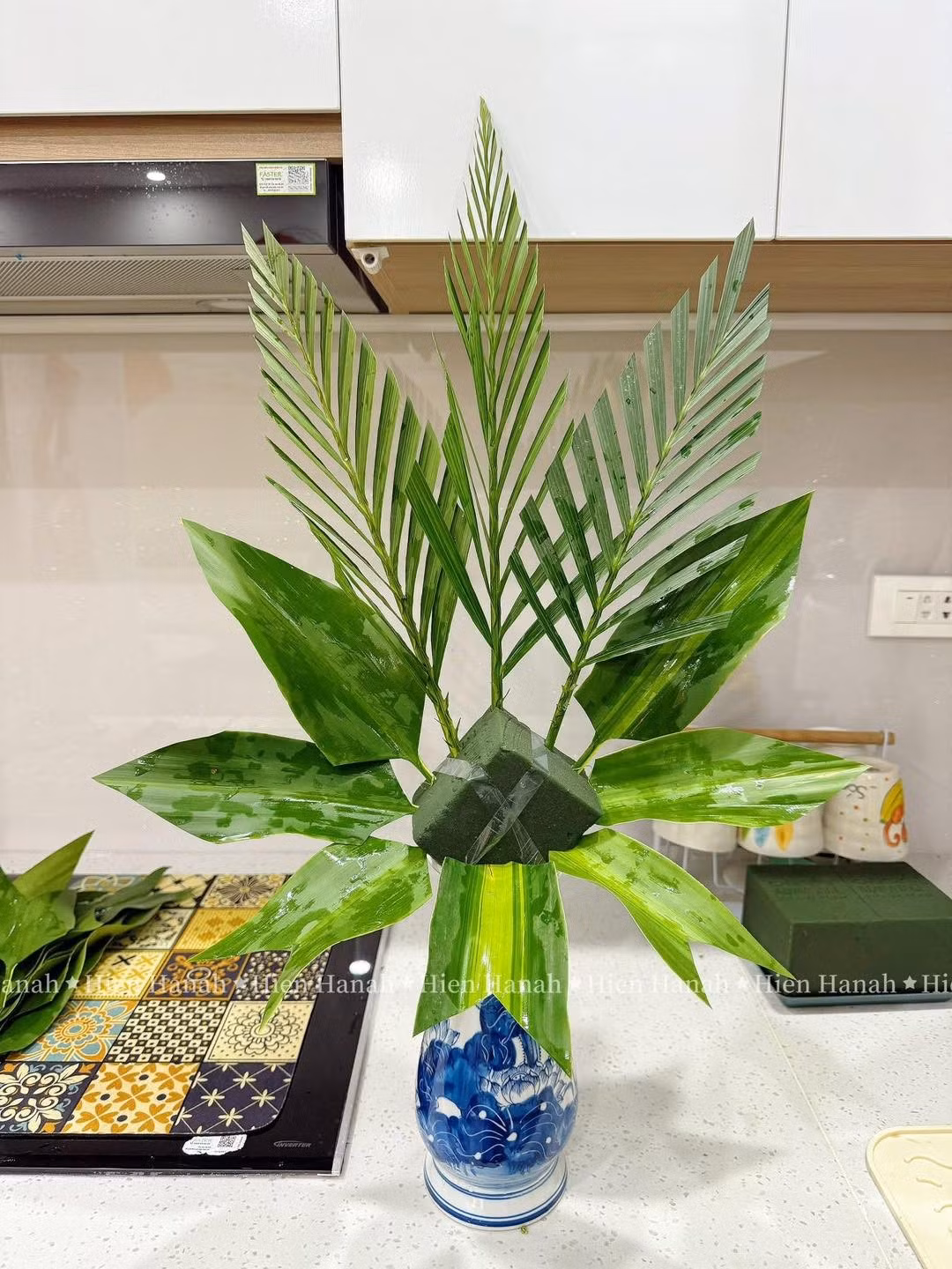 Để có được một bình hoa thờ đẹp mắt, chị em trước tiên sử dụng lá cau hoặc lá phát lộc cắm phía sau và hai bên để tạo khung hình rẻ quạt, mang lại cảm giác sum suê. Tiếp đó, chọn những bông hoa cúc đẹp nhất cắm ở vị trí trung tâm và cao nhất, sau đó cắm thấp dần ra phía trước.