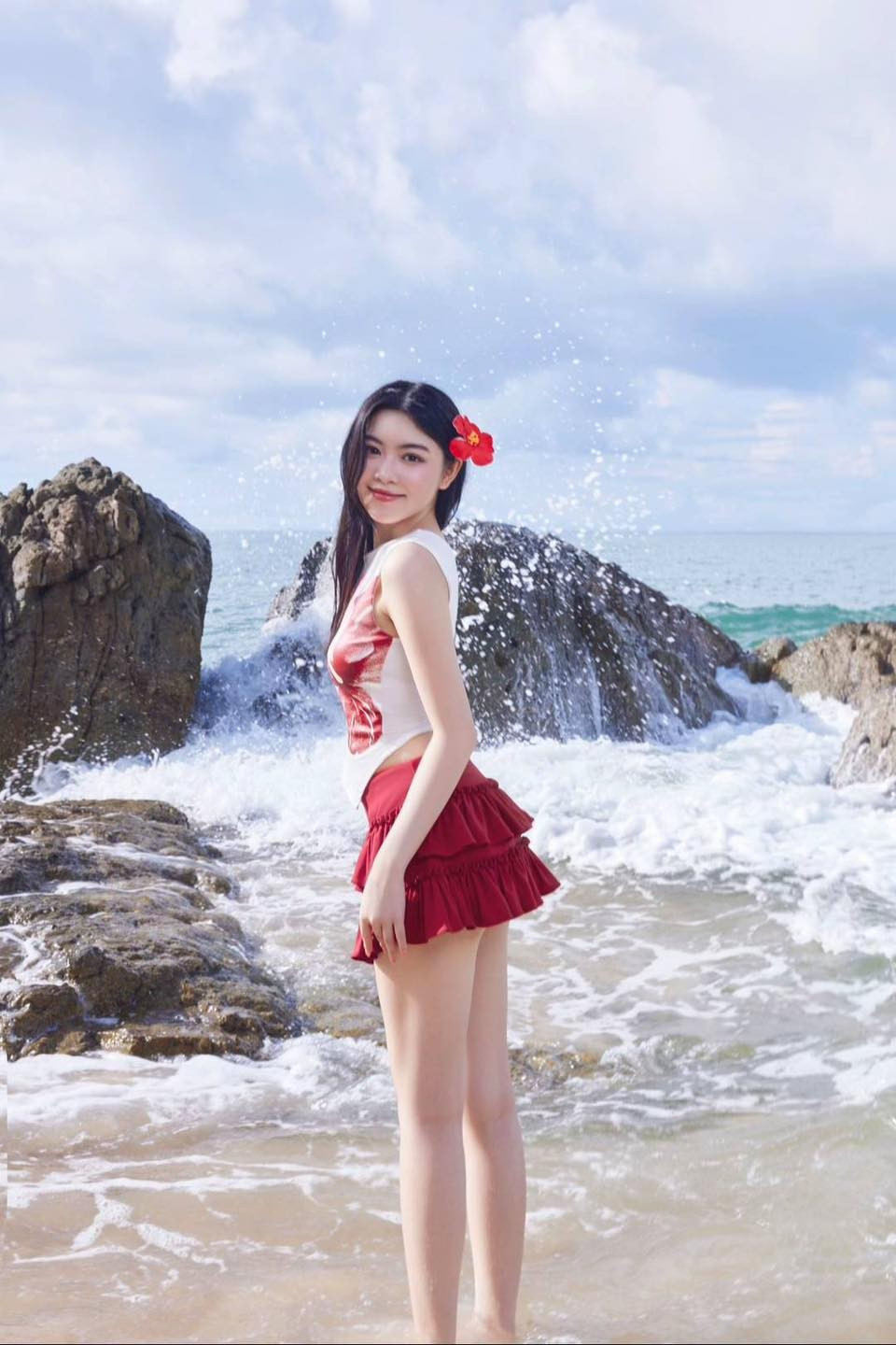 Ở set đồ đầu tiên, Lọ Lem chọn trang phục tông màu đỏ nổi bật với áo crop top trắng in họa tiết hoa hibiscus đỏ rực. Điểm nhấn của set đồ là chiếc chân váy xòe tầng màu đỏ burgundy, tạo nên vẻ nữ tính và dễ thương.