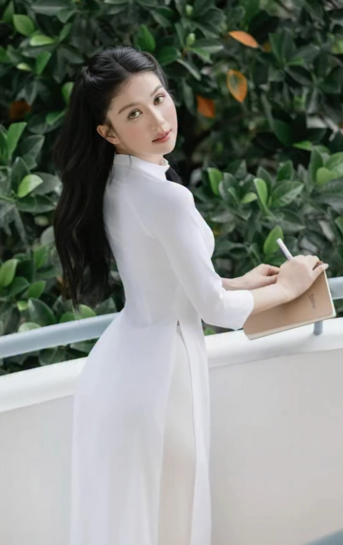 Không dừng lại ở đó, Ngọc Trinh còn diện cả tà áo dài trắng tinh khôi. Cô nhẹ nhàng tạo dáng bên hành lang, mái tóc đen dài xõa tự nhiên càng tôn thêm vẻ đẹp trong trẻo, e lệ.