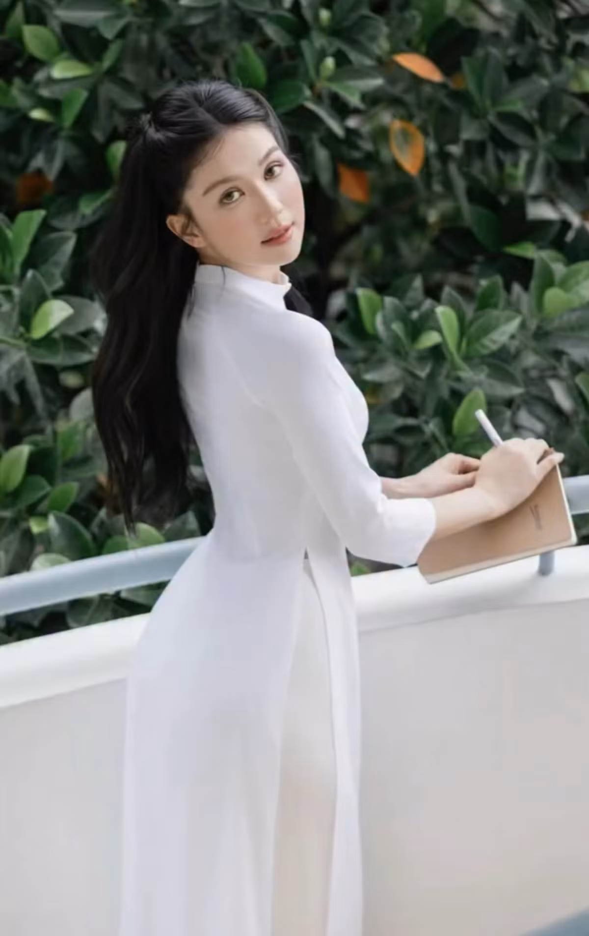 Không dừng lại ở đó, Ngọc Trinh còn diện cả tà áo dài trắng tinh khôi. Cô nhẹ nhàng tạo dáng bên hành lang, mái tóc đen dài xõa tự nhiên càng tôn thêm vẻ đẹp trong trẻo, e lệ.