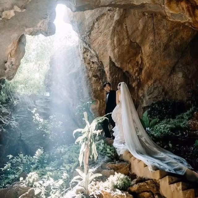 Giữa khung cảnh ấy, cô dâu Katia lộng lẫy trong chiếc váy ren trắng tinh khôi, với chi tiết tay dài và khăn voan thướt tha trải dài trên nền cỏ xanh và bậc đá, tạo nên hình ảnh một nàng thơ bước ra từ câu chuyện cổ tích.(Ảnh: Niên và Katia)