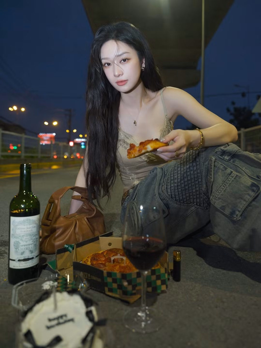 Trong một khoảnh khắc khắc, nữ diễn viên một tay cầm ly rượu vang, tay kia nâng miếng pizza, cô nàng không ngần ngại thể hiện cá tính tự do và tinh thần “ăn mừng theo cách của riêng mình”. Chiếc bánh sinh nhật nhỏ xinh cùng dòng chữ “Happy Birthday” như một điểm nhấn nhẹ nhàng, ngọt ngào giữa tổng thể phá cách.