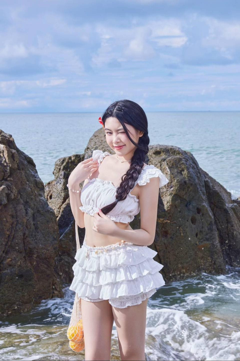 Tóc được tết bím sang một bên, kết hợp với chiếc kẹp tóc đỏ nhỏ xinh làm điểm nhấn.