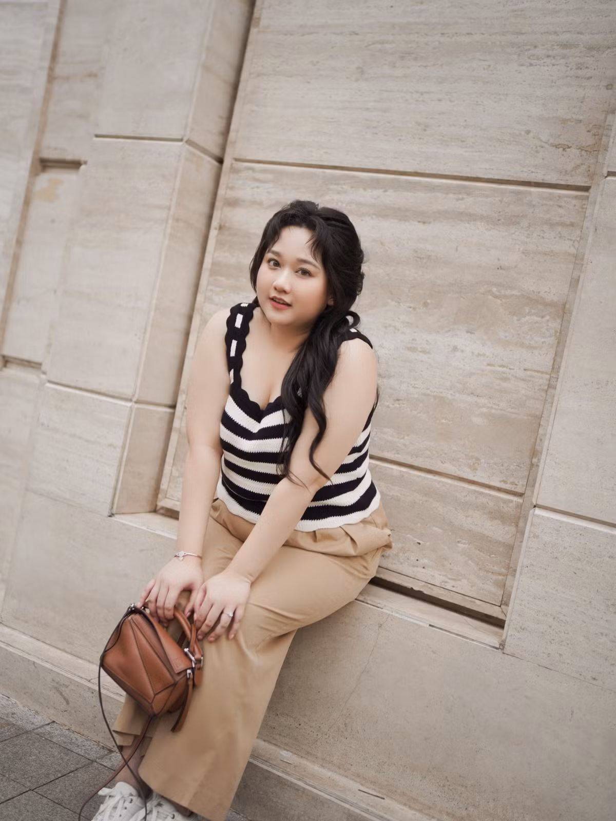 Cô kết hợp thêm chiếc túi xách da nâu nhỏ xinh và đôi giày thể thao trắng, tạo nên tổng thể năng động, trẻ trung.