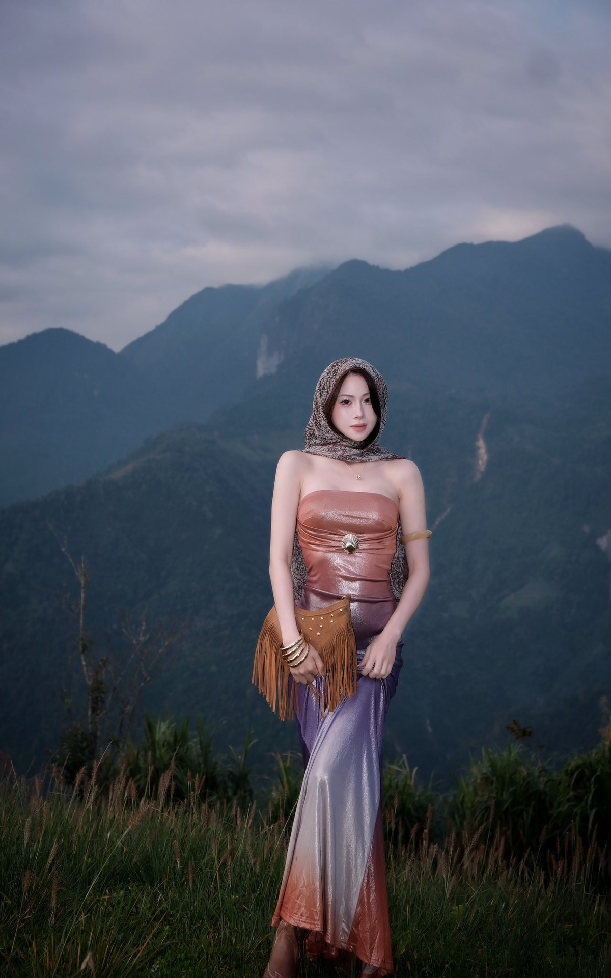 Cô gái diện một chiếc đầm quây bó sát, có hiệu ứng chuyển màu kim loại lấp lánh từ nâu đồng ở phần thân trên sang tím hoặc xanh tím ở chân váy. Chất liệu này tạo cảm giác vừa hiện đại, vừa phảng phất nét huyền bí. (Ảnh: FBNV)