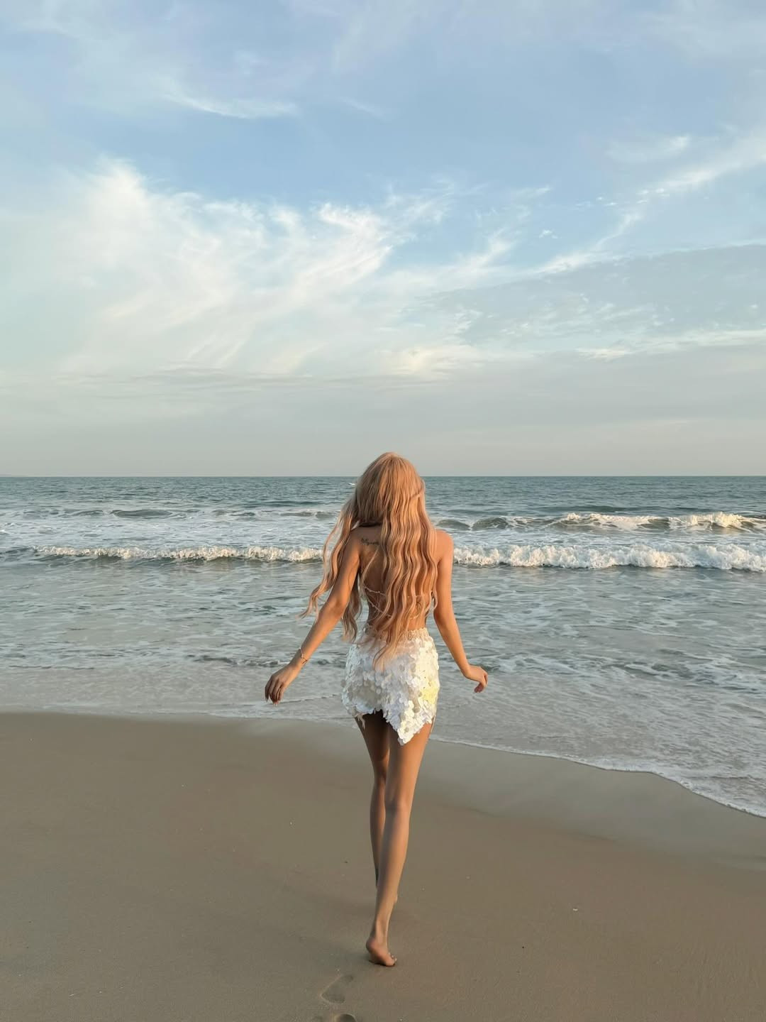 Dù đứng trước khung cảnh biển xanh sóng vỗ dập dìu, nhan sắc của nữ DJ sinh năm 1996 vẫn là tâm điểm của mọi ánh nhìn. Mái tóc vàng bạch kim uốn lượn sóng dài ngang lưng càng làm tăng thêm vẻ "thần tiên" cho bộ ảnh. (Ảnh: IGNV)