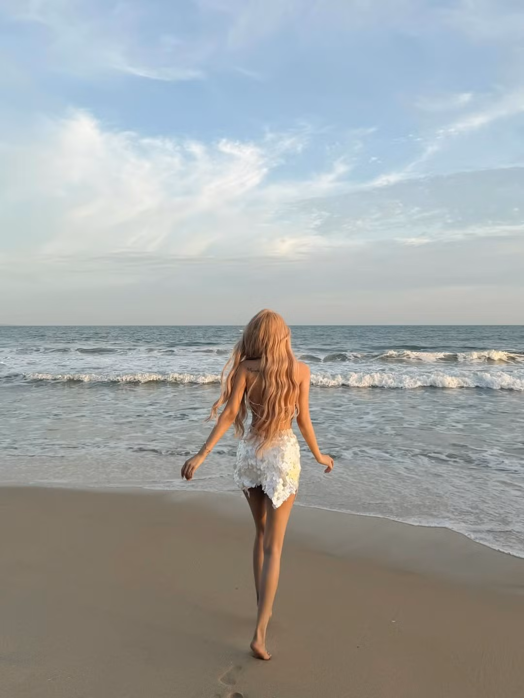 Dù đứng trước khung cảnh biển xanh sóng vỗ dập dìu, nhan sắc của nữ DJ sinh năm 1996 vẫn là tâm điểm của mọi ánh nhìn. Mái tóc vàng bạch kim uốn lượn sóng dài ngang lưng càng làm tăng thêm vẻ "thần tiên" cho bộ ảnh. (Ảnh: IGNV)