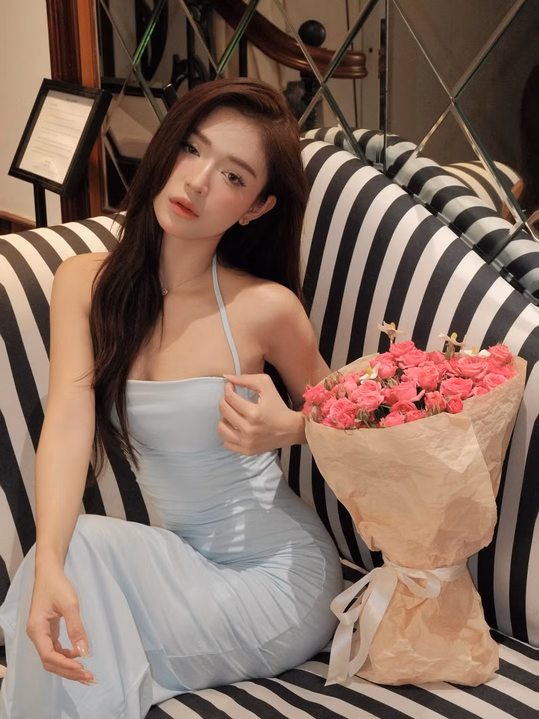 Sắc hồng rực rỡ của hoa hòa quyện cùng màu xanh pastel của váy và bối cảnh đậm chất châu Âu tại một nhà hàng, tạo nên không khí vô cùng ngọt ngào và thơ mộng. (Ảnh: IGNV)