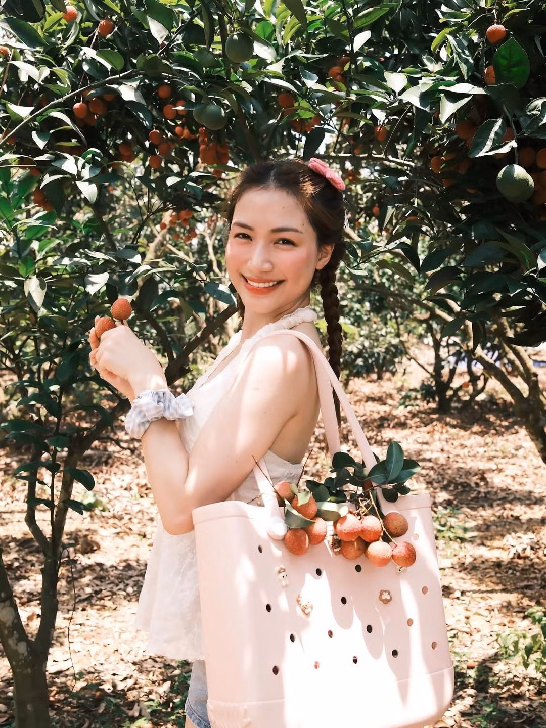 Mái tóc dài được tết hai bên gọn gàng, tô điểm thêm chiếc kẹp tóc hình nơ màu hồng và chiếc scrunchie xinh xắn, càng làm tăng thêm nét trẻ trung, đáng yêu.