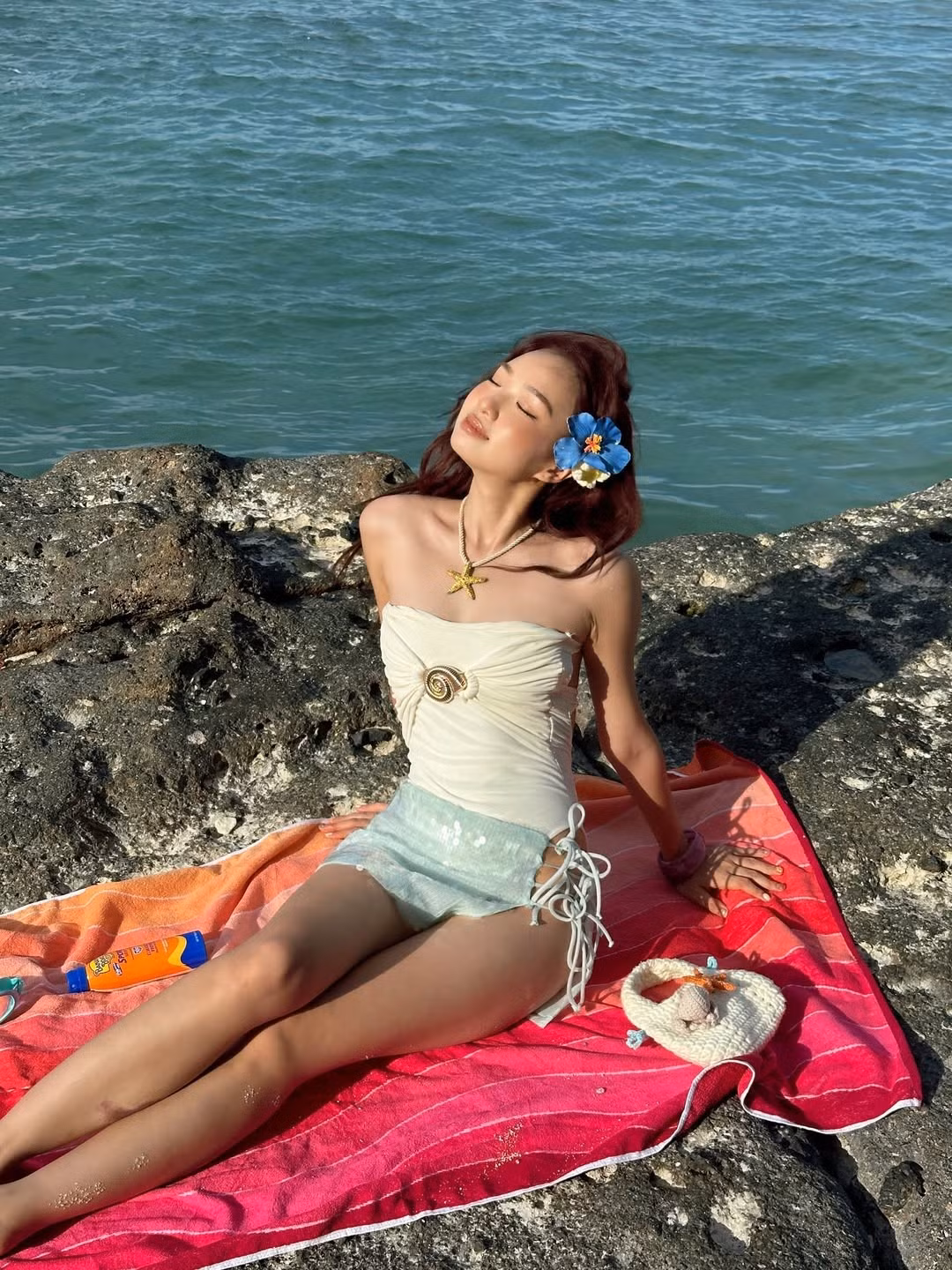 Điểm nhấn của bộ trang phục chính là chiếc vòng cổ hình sao biển và chiếc khăn quấn hông lấp lánh sắc xanh ngọc, mô phỏng vây cá, tạo nên hình ảnh một nàng tiên cá hiện đại và đầy quyến rũ.