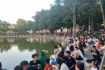 Khoảng 17h chiều không khí quanh khu vực Hồ Gươm bắt đầu nhộn nhịp khi các gia đình và nhóm bạn trẻ chủ động tới sớm để chọn vị trí quan sát thuận lợi nhất. Nhiều người dân cẩn thận chuẩn bị quạt mát vật dụng cá nhân và tranh thủ nghỉ ngơi trong lúc kiên nhẫn chờ đợi nhiều giờ trước thời điểm pháo hoa khai màn. (Ảnh: Anh Sơn)