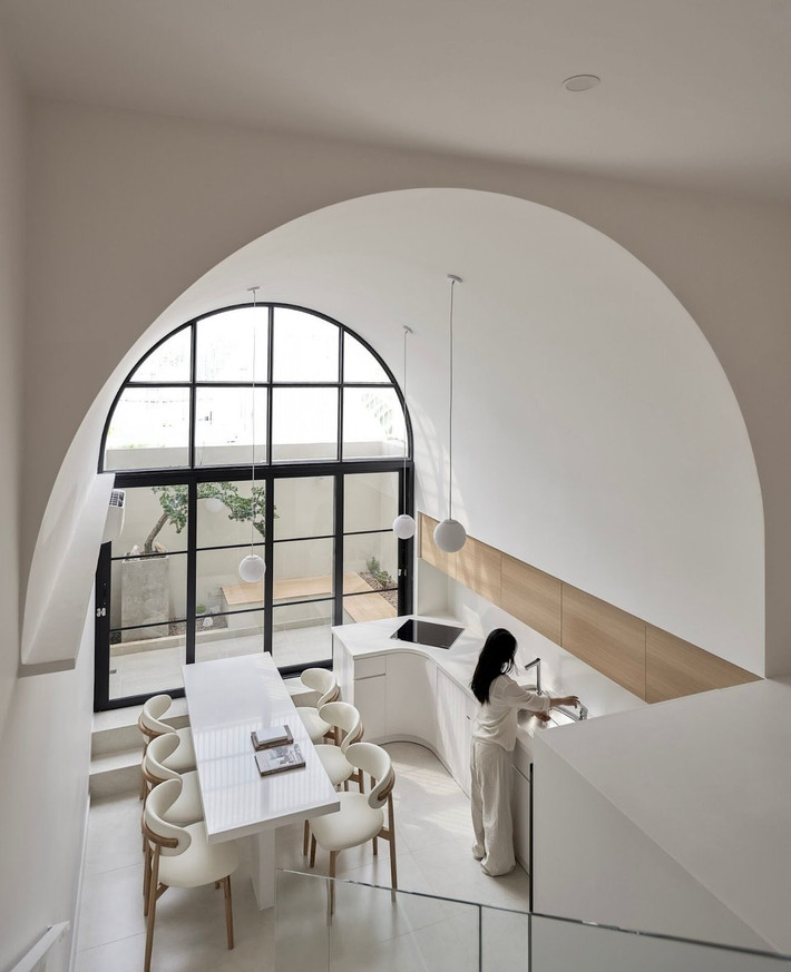 Trong khi nhiều nhà phố đặt phòng khách làm trung tâm, thì White Oasis tái định vị bếp và bàn ăn thành “linh hồn” của công trình. Một khoảng vòm cao xuyên tầng được mở ra, kết hợp bề mặt kính lớn giúp ánh sáng tràn ngập không gian. Ảnh: Phú Đào
