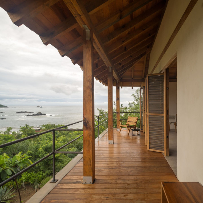 Ban công gỗ với ghế mây thư giãn đặt cạnh lan can kim loại tối giản. Ảnh: Archello