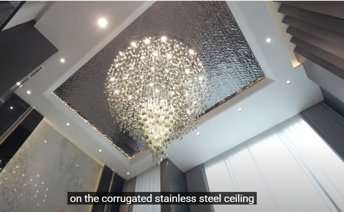 Điểm nhấn trong phòng khách là bộ đèn chùm hoành tráng trên nền trần inox dập sóng. Ảnh chụp màn hình NhaF