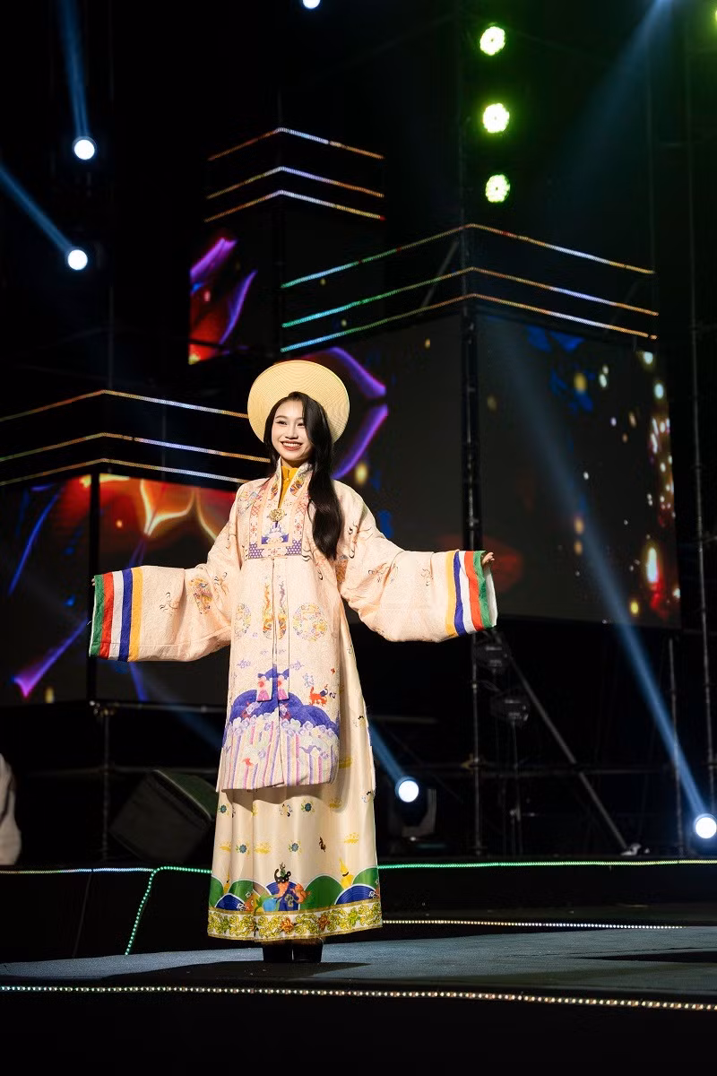 Màu sắc chủ đạo của bộ sưu tập là các gam màu quý tộc như xanh ngọc, đỏ son, vàng kim – vừa tôn vinh vẻ đẹp của người mặc, vừa gợi nhớ hình ảnh trang nghiêm, cao quý của Hoàng hậu Nam Phương khi xưa. Dải cổ áo viền thêu tinh xảo, tay áo rộng phủ nhẹ như cánh phượng, các đường kẻ sọc ngũ sắc nơi vạt áo là điểm nhấn đặc trưng của áo Nhật Bình. Mỗi chi tiết đều được chăm chút tỉ mỉ, phản ánh trình độ thủ công tinh hoa và niềm đam mê gìn giữ di sản văn hóa của nhà thiết kế.