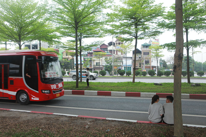 Một nhóm bạn trẻ đứng, ngồi bên mép đường chụp ảnh khi có rất nhiều tải, xe khách chạy với tốc độ cao qua đây.