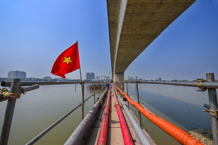 Một cây cầu tạm được thi công để đưa công nhân và vật liệu ra thi công ở giữa sông Hồng. Trước đó, nhà thầu phải thuê một cơ quan phụ trách phân luồng tàu bè, đảm bảo an toàn giao thông đường thủy qua khu vực.