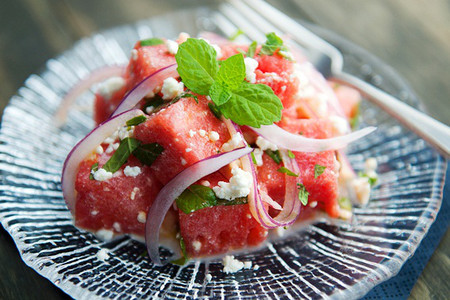 Salad dưa hấu. Nguyên liệu: 1 /2 quả dưa hấu, 1 quả hành tây, ít lá bạc hà, chanh, dầu olive, 1 ít phô mai vụn. Dưa hấu gọt vỏ, cắt miếng vuông vừa ăn. Hành tây xắt lát mỏng. Nếu sợ hành quá hăng bạn có thể ngâm vào tô nước đá lạnh khoảng 15 phút rồi vớt ra, để ráo. Cho hành và dưa hấu vào tô, thêm phô mai và lá bạc hà xắt nhỏ. Rưới dầu olive và nước chanh vào tô salad, trộn đều.
