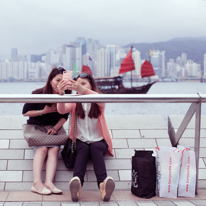 Bộ ảnh này chụp tại dọc Đại lộ Ngôi sao ở Hồng Kông, là một địa điểm nổi tiếng mà rất dễ bắt gặp những hình ảnh như thế này. Các cô gái trẻ tay giơ điện thoại và làm dáng để "tự sướng".
