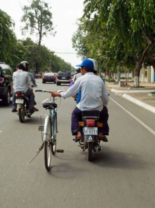 Ngồi sau xe máy, tay dắt xe đạp.