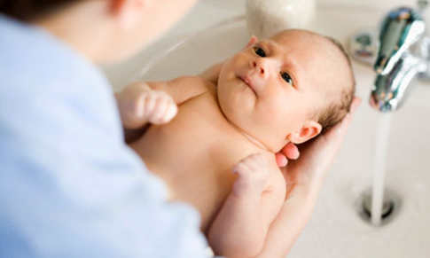 Một tay mẹ nâng cao gáy của con lên để nước không rơi vào mắt bé. Tay còn lại dùng khăn ẩm xoa đầu cho bé cho tới khi hết dầu gội và tóc bé sạch sẽ. Cuối cùng, xả lại cho thật sạch dưới vòi nước ấm.