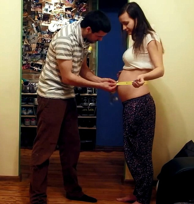 Người chồng đang dùng thước dây đo sự thay đổi kích thước bụng vợ.