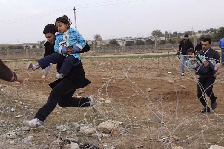 Những người tị nạn Syria ở thị trấn Ras al-Ain nhảy qua hàng rào dây thép gai chạy sang Thổ Nhĩ Kỳ. Những người tị nạn Syria ở thị trấn Ras al-Ain nhảy qua hàng rào dây thép gai chạy sang Thổ Nhĩ Kỳ.