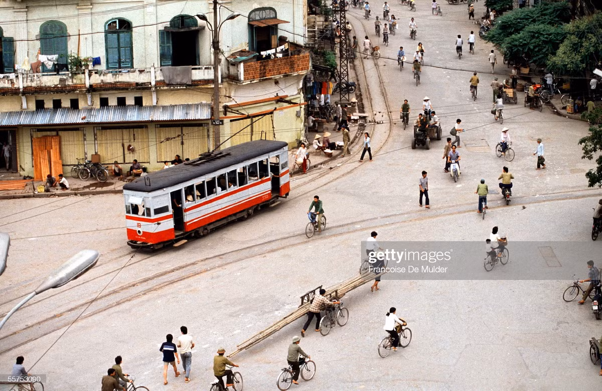 Tàu điện từ phố Hàng Gai chạy vào ngã năm Bờ hồ. Một xe công nông chạy phía sau.