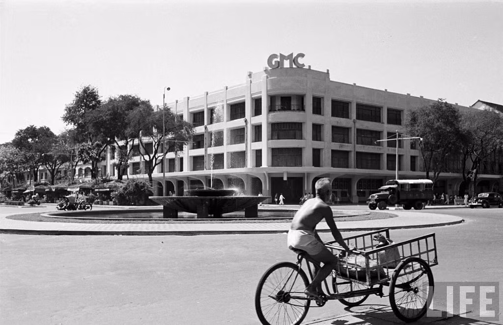 Chiếc xe ba gác chạy qua giao lộ Bonard - Charner (Lê Lợi - Nguyễn Huệ), bên kia đường là tòa nhà Les Grands Magazins Charner (GMC), sau này là Thương xá TAX.