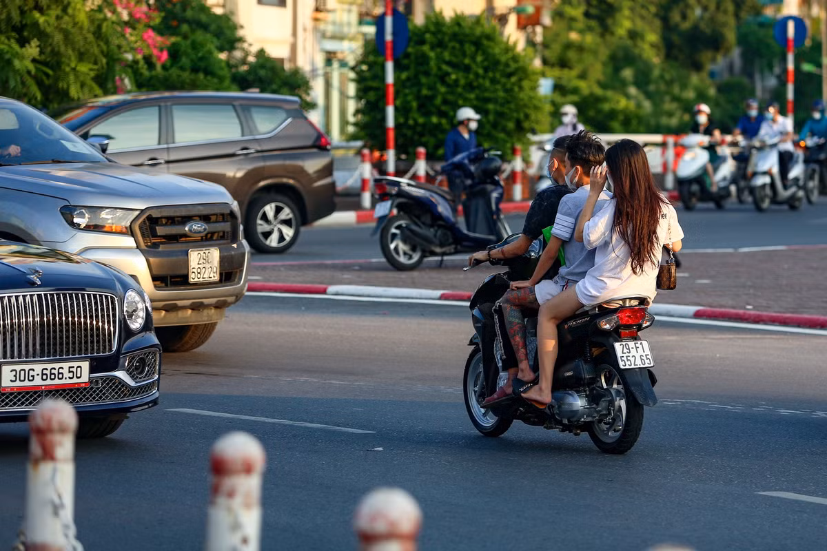 Một chiếc xe máy chở 3 người không đội mũ bảo hiểm bất chấp nguy hiểm đi lách qua nhiều ôtô để sang làn đường bên kia.