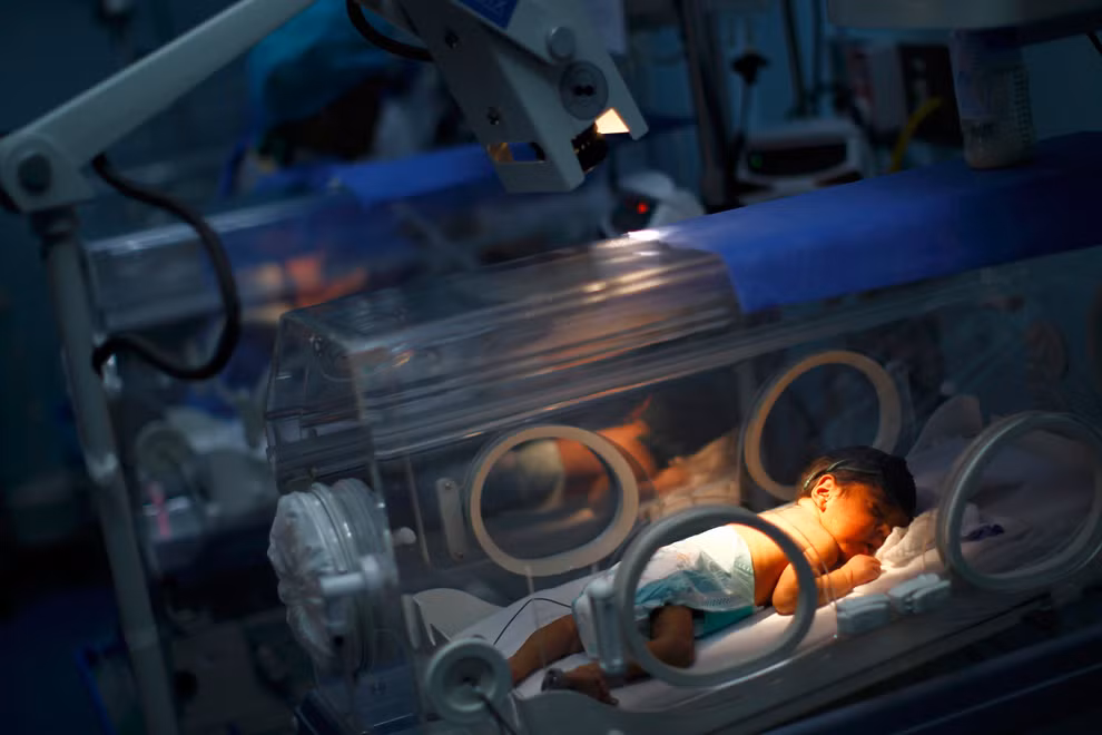 Một em bé sơ sinh nằm ngủ bên trong lồng ấp trong lúc được chăm sóc sức khỏe bằng liệu pháp ánh sáng.