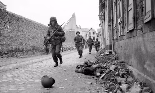Binh sĩ Mỹ vội vã di chuyển ở Coblenz, Đức ngày 18/3/1945. Thi thể một binh sĩ tử trận nằm bên vệ đường.