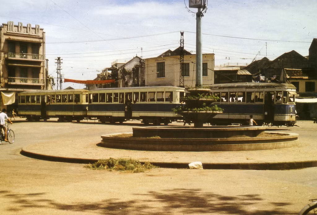 Tàu điện chạy ngang qua đài phun nước ở ngã năm bờ hồ, 1974. Tòa nhà có dòng chữ M.D.Q.D phía trái là mậu dịch quốc doanh. Ảnh: Günter Mosler.