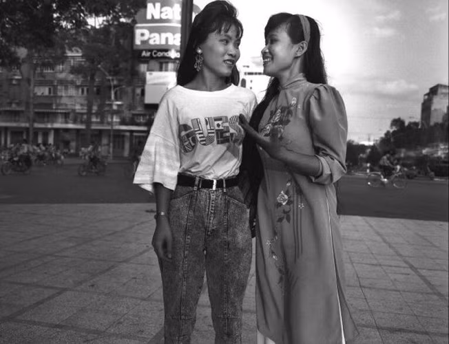Hai thiếu nữ, một người mặc áo dài truyền thống, người kia mặc quần bò áo phông tán gẫu trên đường phố ở TP HCM, 1992. Ảnh: Raymond Depardon/ Magnum Photos.