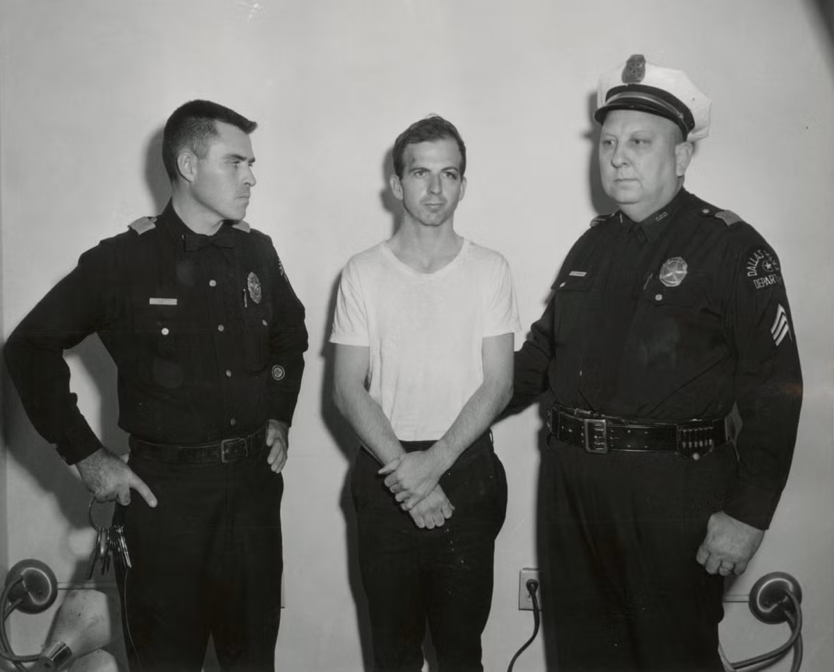 Lee Harvey Oswald, kẻ bị buộc tội ám sát Tổng thống Kennedy, trong bức ảnh chụp cùng 2 sĩ quan cảnh sát Dallas.Theo các cuộc điều tra của chính phủ liên bang, sĩ quan cảnh sát Dallas J. D. Tippit đã bị Lee Harvey Oswald bắn chết ở khu phố Oak Cliff sau khi Tippit chặn Oswald lại để thẩm vấn ngay sau vụ ám sát. Oswald, cựu lính thủy quân lục chiến, bị bắn chết ở tầng hầm của Sở cảnh sát Dallas 2 ngày sau khi Tổng thống Kennedy bị giết.