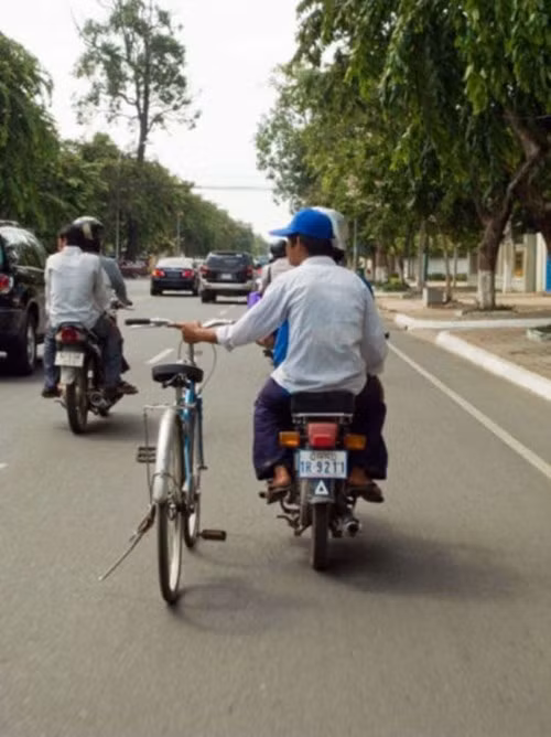 Ngồi sau xe máy, tay dắt xe đạp.