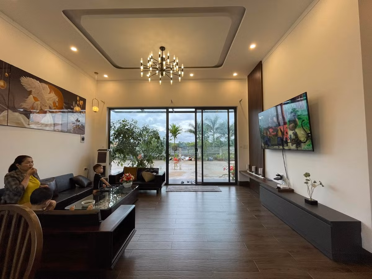 Nhà có nền khá cao, phía trước bậc tam cấp làm rộng để các cháu có chỗ ngồi chơi, hóng gió. Hai bên là cây cảnh, hoa rực rỡ quanh năm. Khung cửa kính lớn giúp người lớn ở trong nhà vẫn để ý được trẻ con đang chơi bên ngoài.