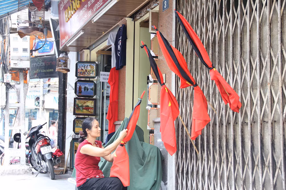 Người phụ nữ ngồi buộc, bán cờ rủ trên phố Hàng Bông