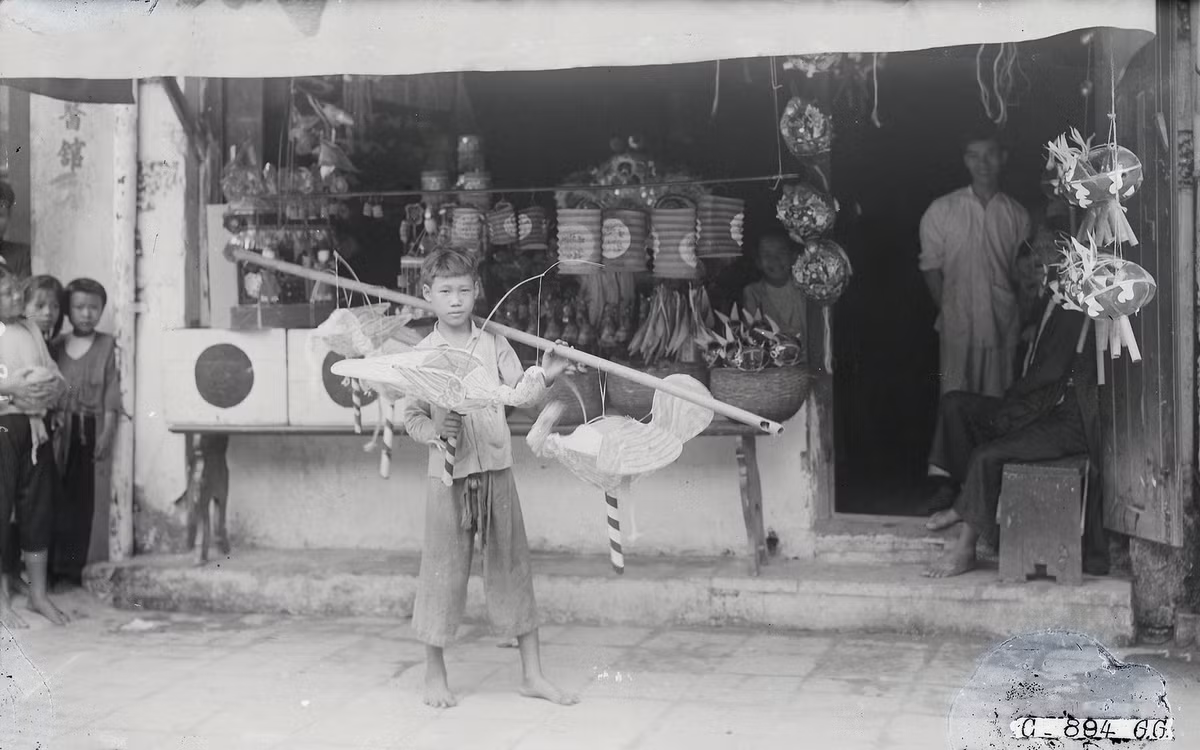 Một cậu bé cầm đèn lồng đứng chào hàng cho cửa hàng của nhà mình.