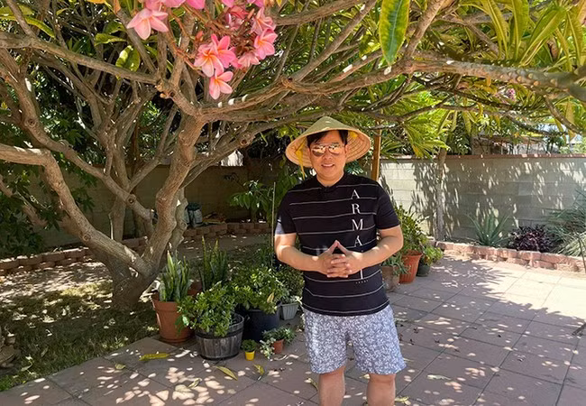 Quang Lê đeo kính đen, đội nón lá ra làm vườn ở Mỹ. Nam ca sĩ vừa tiêm xong vắc-xin phòng Covid-19.