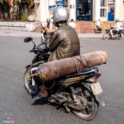 Đằng sau người đàn ông này là một bình gas cũ kĩ, gỉ sét.