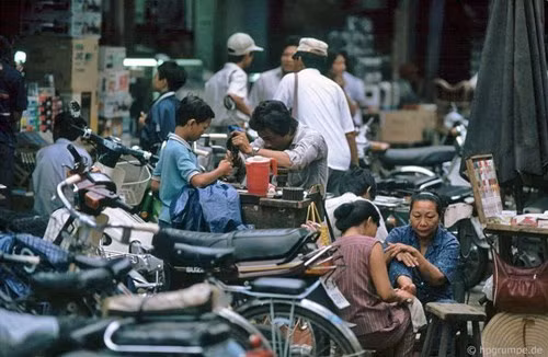 Một bà bán thuốc lá đang tán gẫu với bạn trong khi người thợ sửa khóa gần đó miệt mài với công việc của mình.