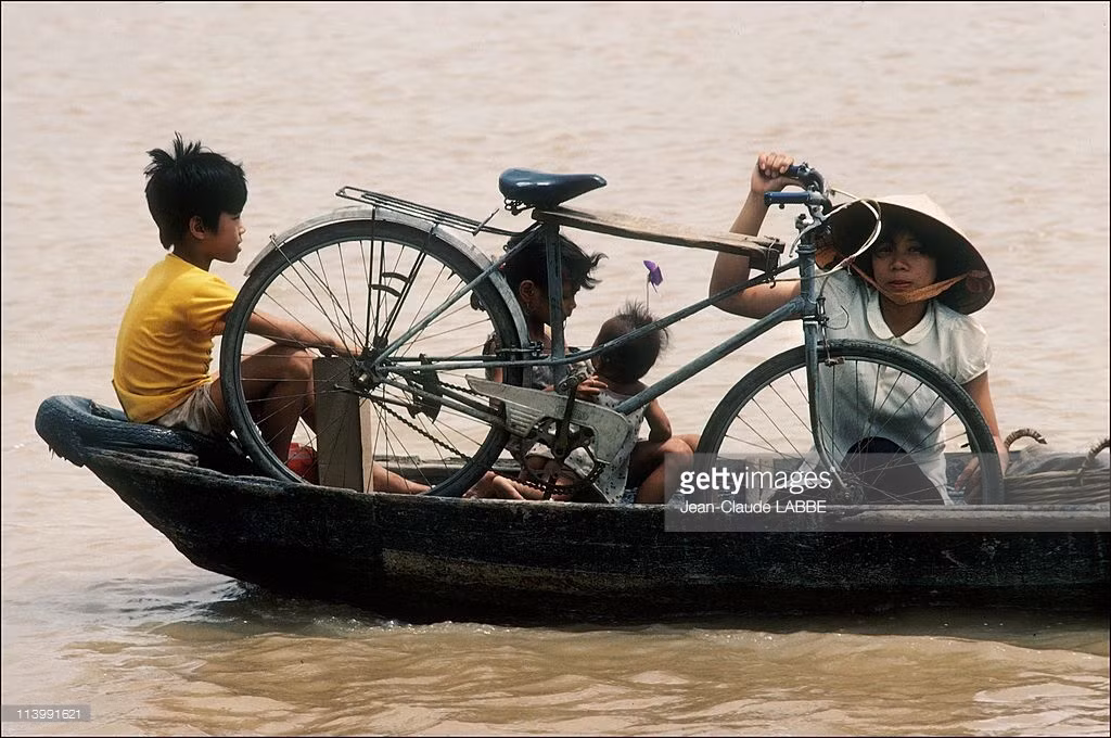 Người mẹ và những đứa con nhỏ cùng chiếc xe đạp qua sông trên một chuyến đò.