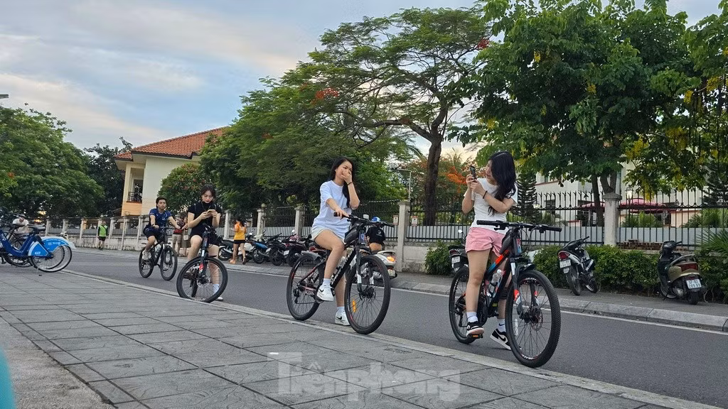 Các bạn trẻ đạp xe tập thể dục dừng chân ngắm vẻ đẹp hoàng hôn khi mặt trời lặn xuống phía bên kia mặt hồ.